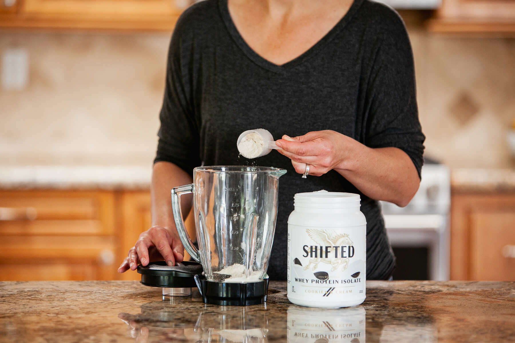 Woman pouring a scoop of protein powder into a blender