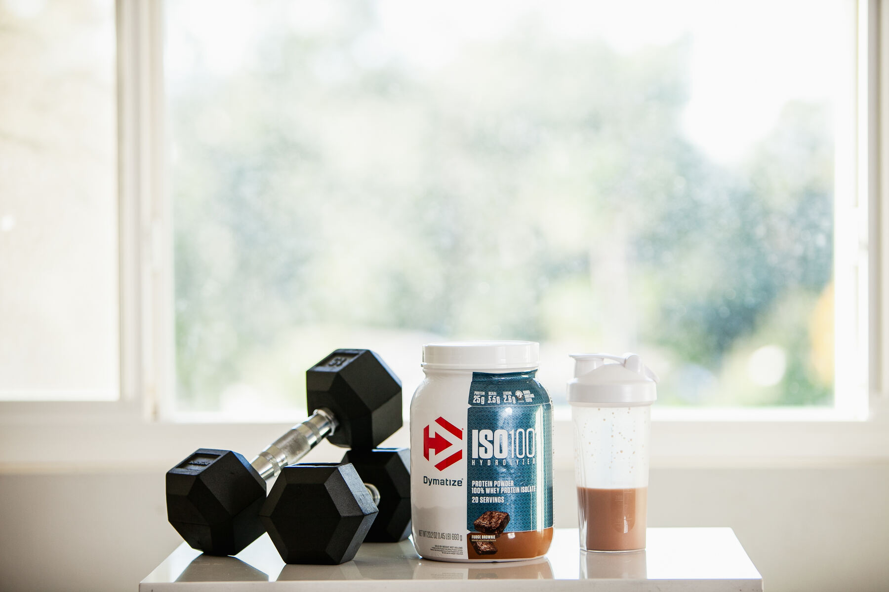 Dynamize ISO 100 bottle with a pair of dumbbells and a water bottle filled with protein shake