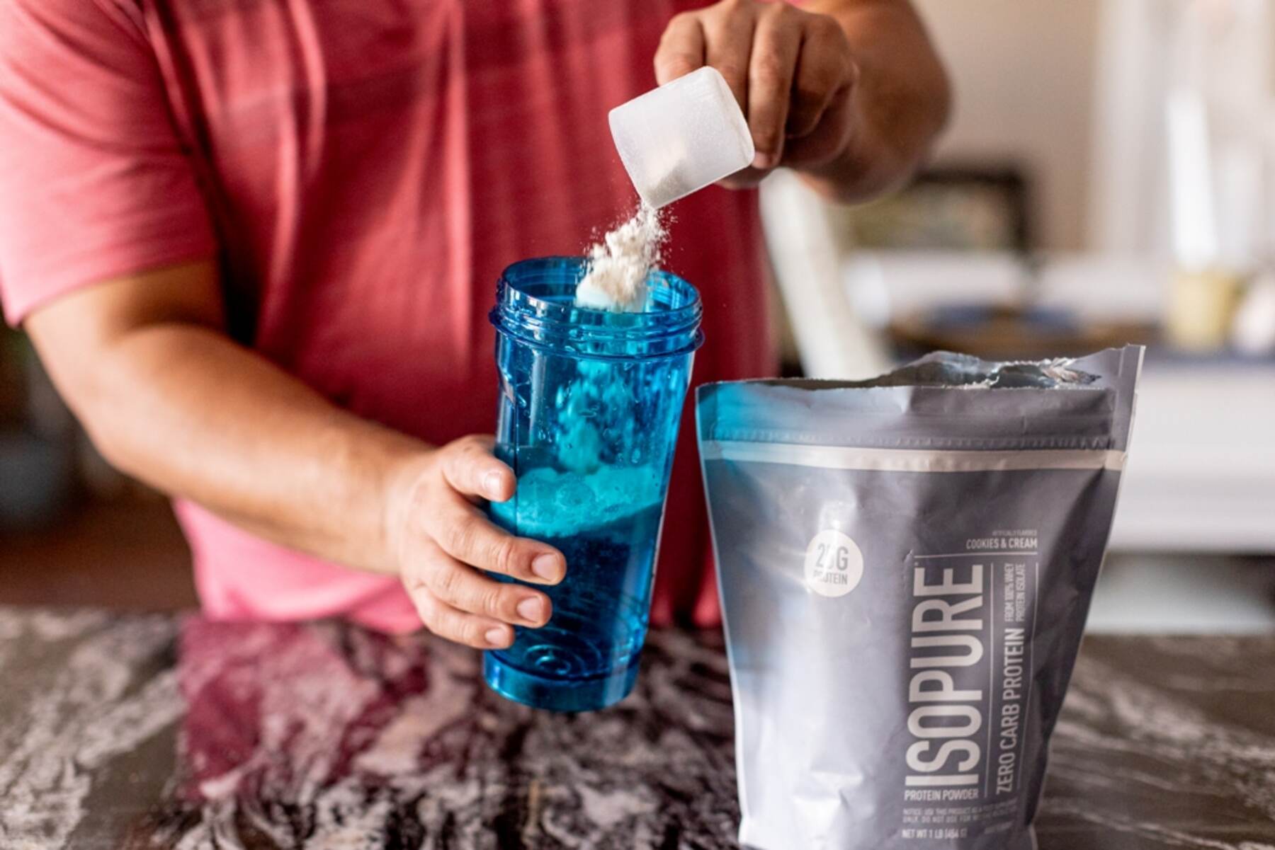 Man taking a scoop of ISOPURE Zero Carb Protein powder in a water bottle