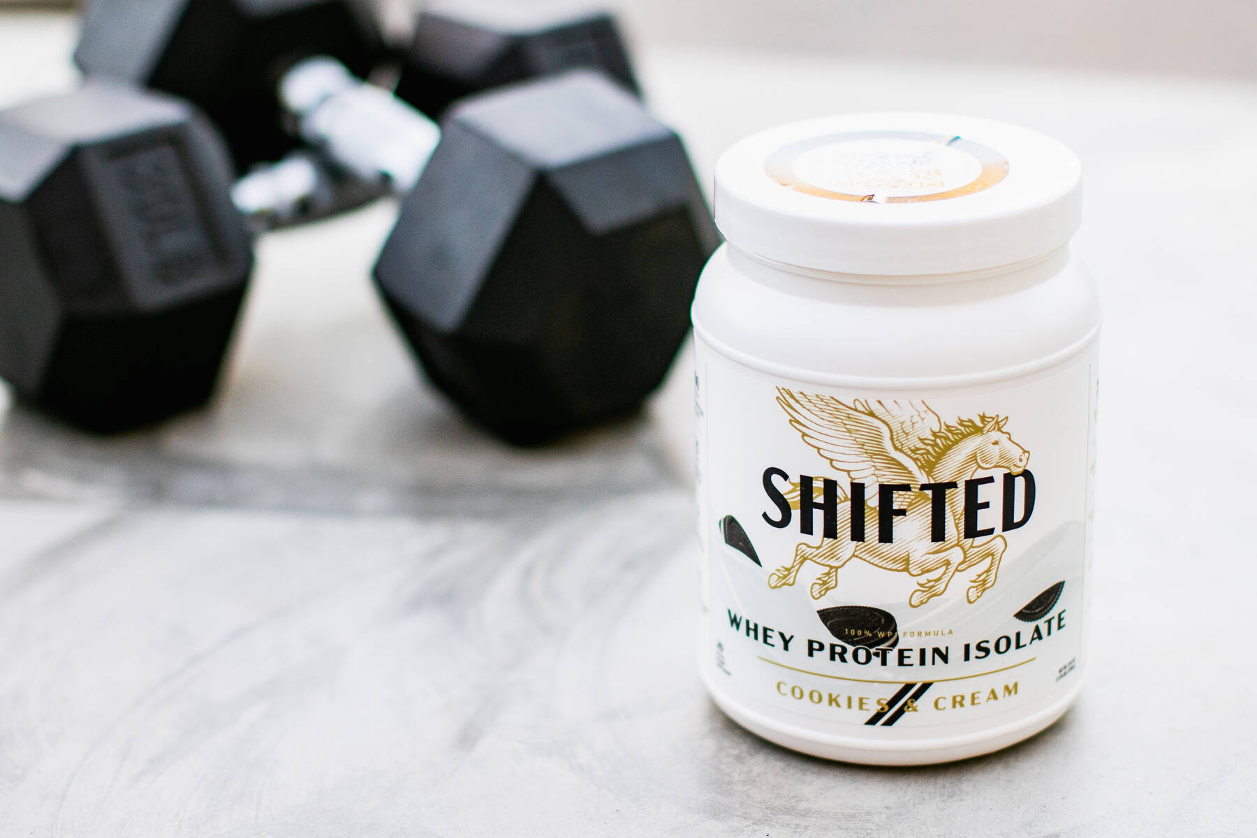 Shifted Whey Protein Isolate with dumbbells on the background