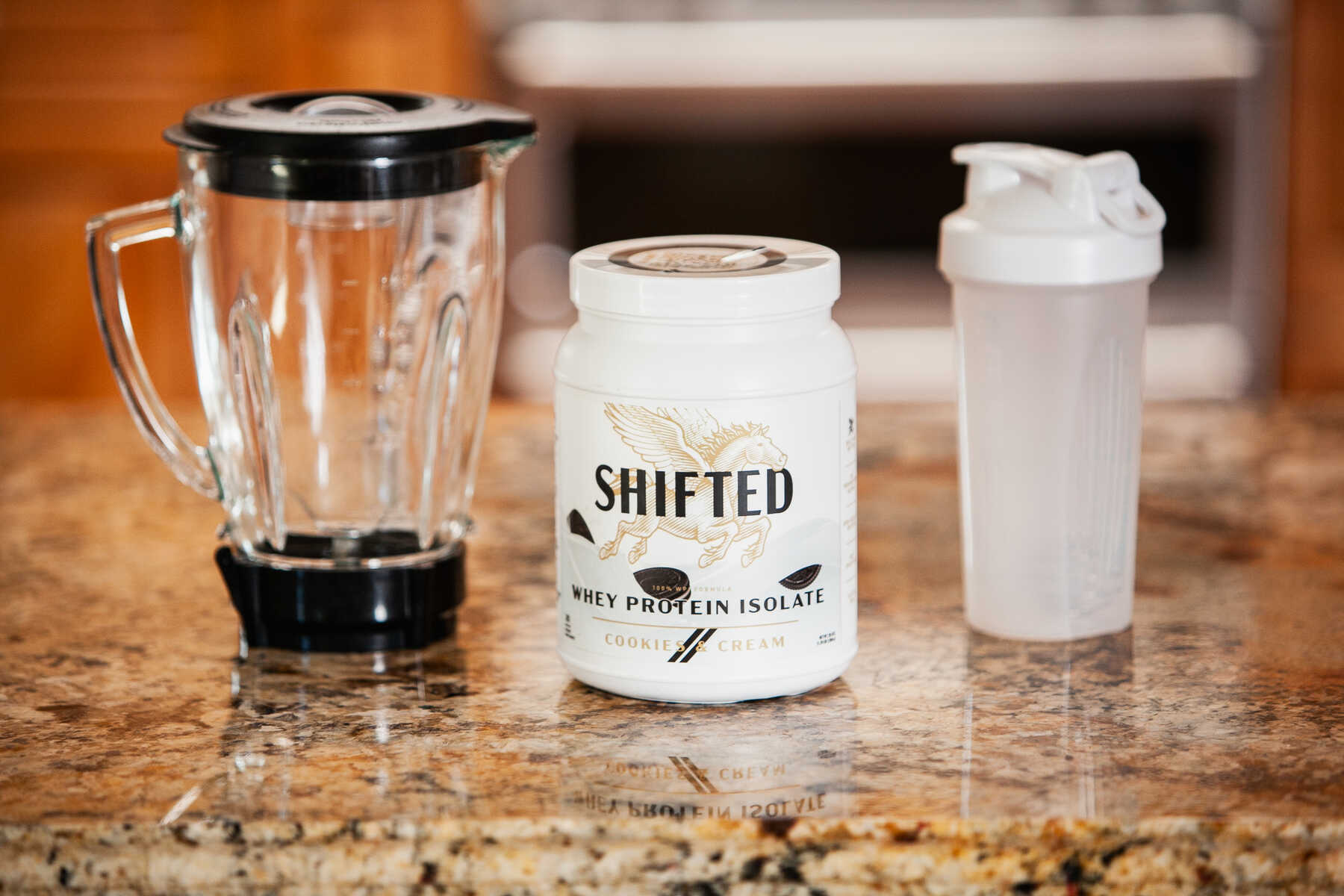 Shifted Whey Protein Isolate powder beside a blender and an empty water bottle