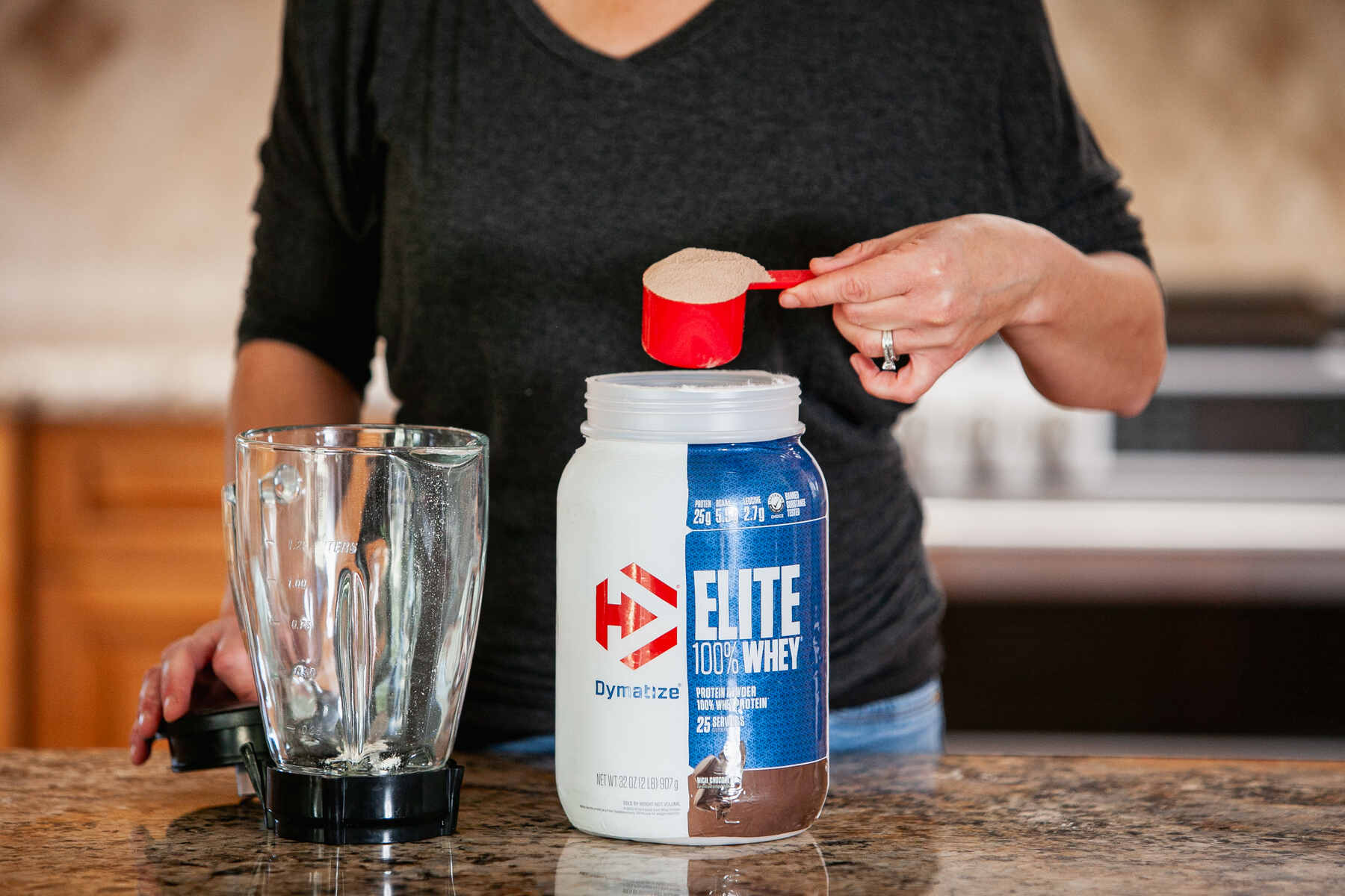 Woman taking out a scoop of Elite 100% whey protein powder