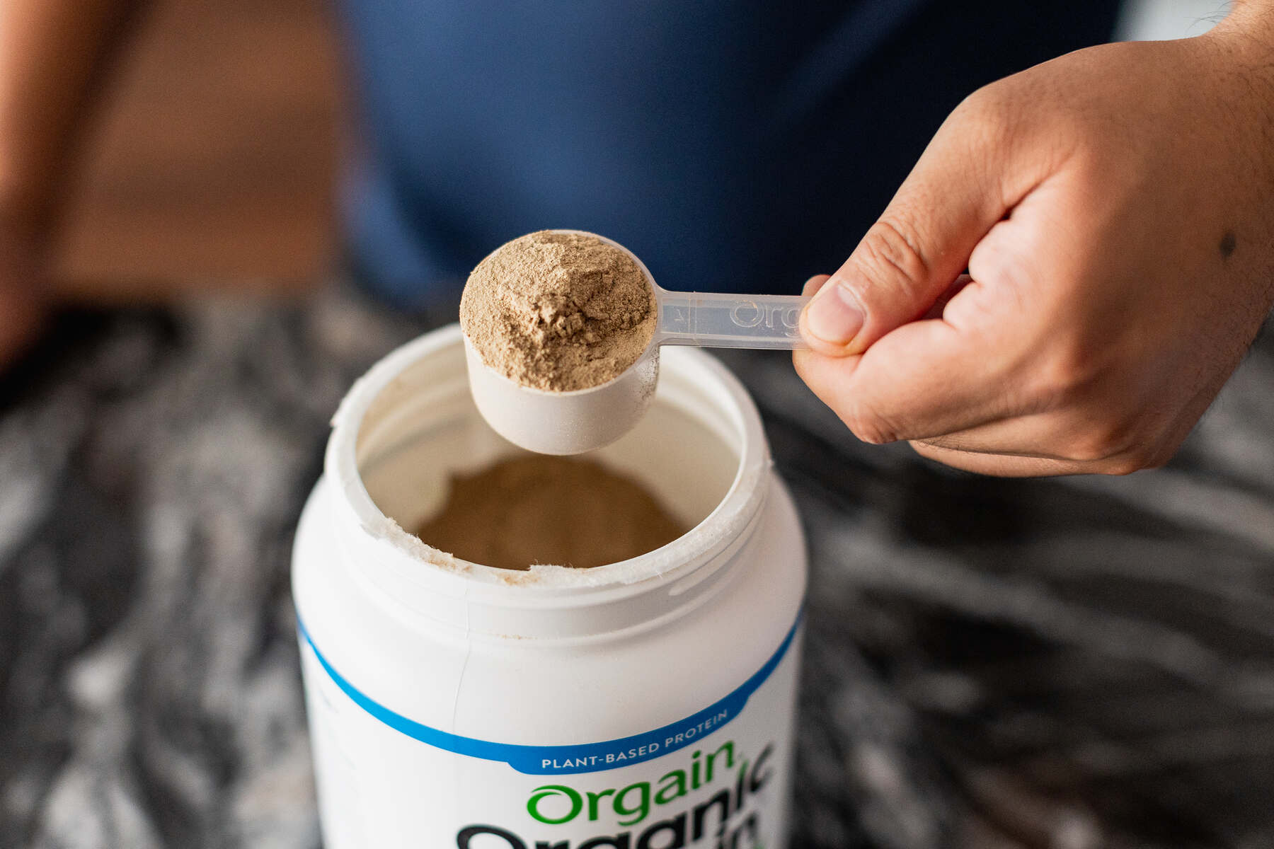 Person scooping protein powder from a bottle