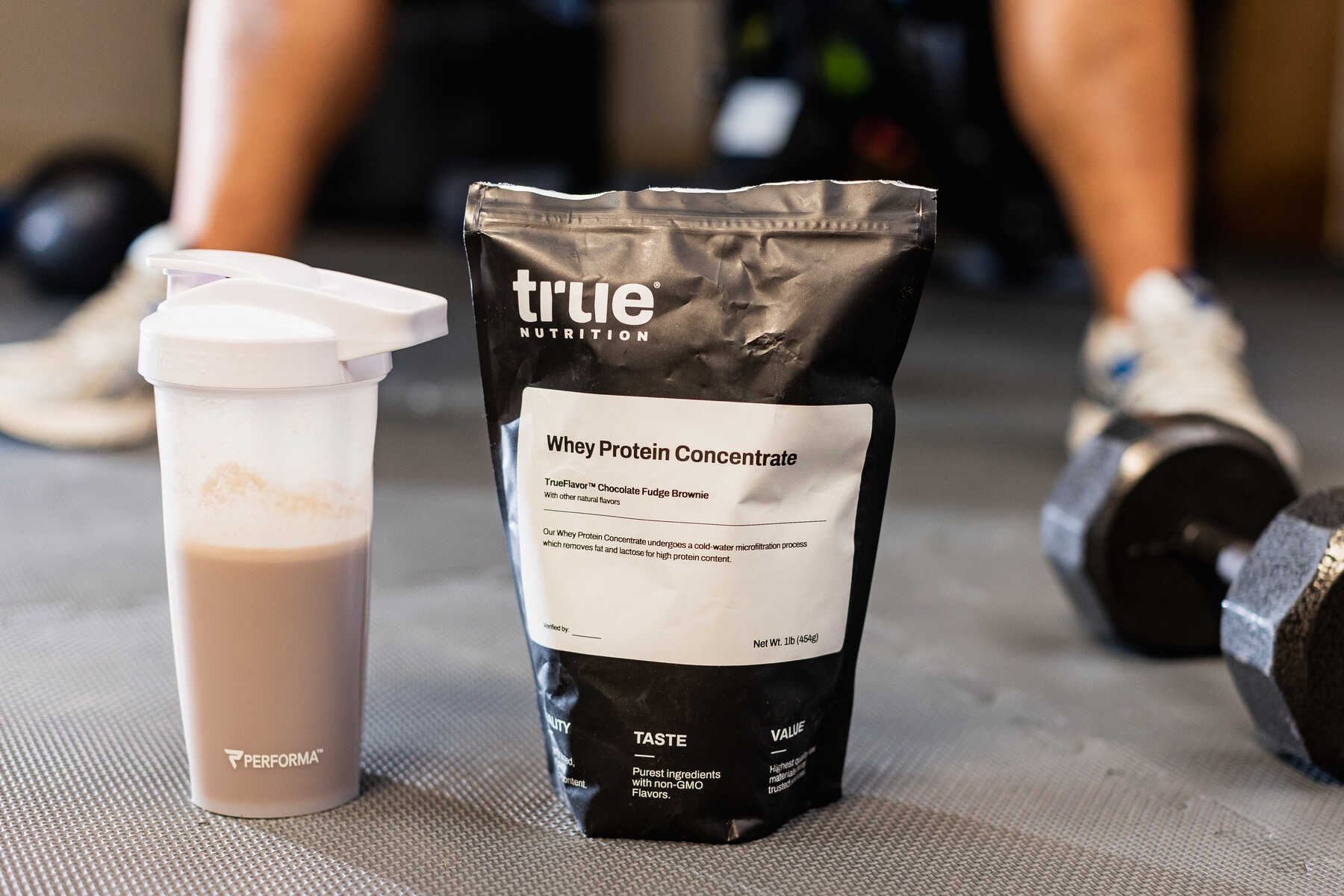 Close up of True Whey Protein Powder beside a water bottle filled with protein shake