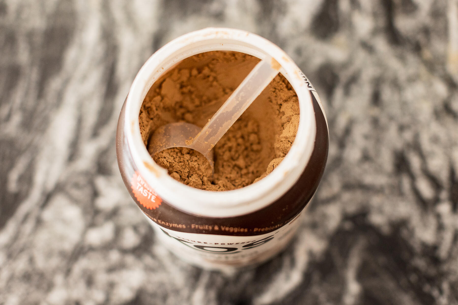 Open container of chocolate protein powder with a clear scoop sitting inside of it
