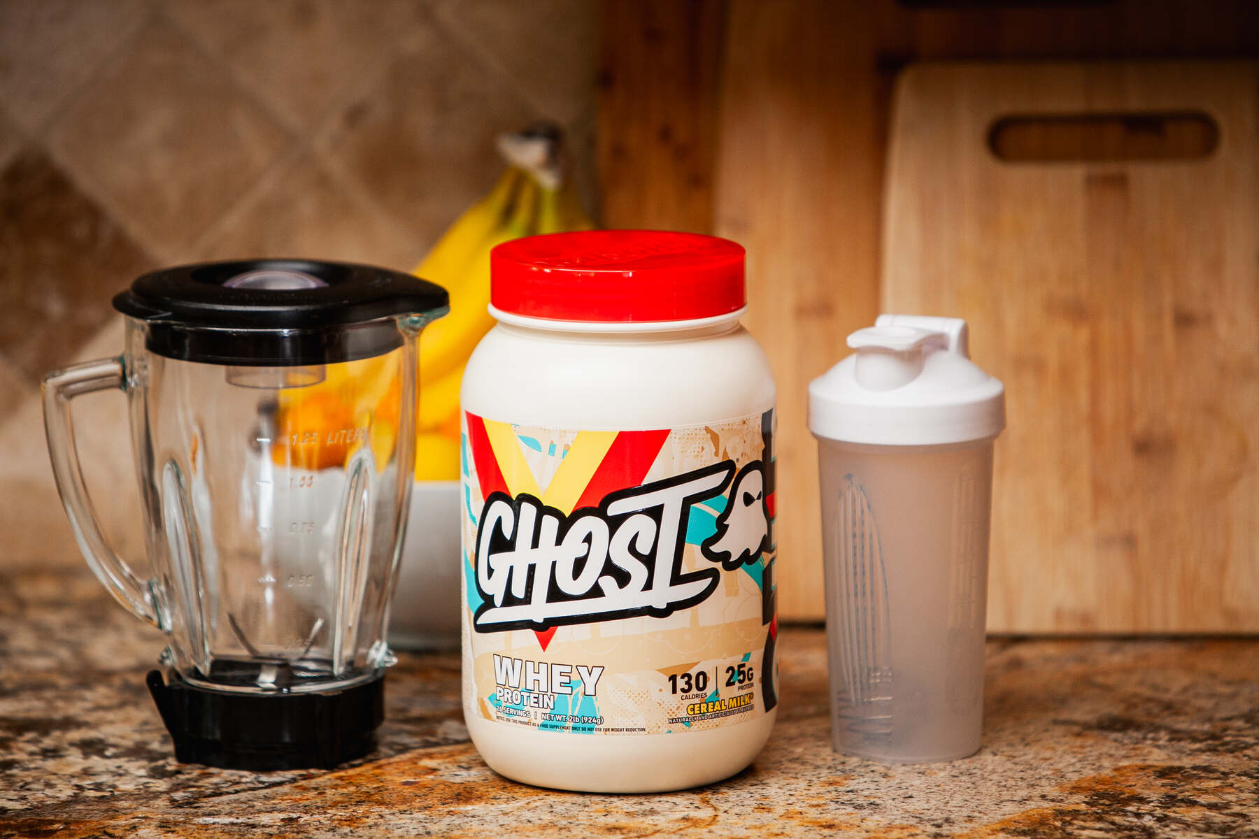 A protein powder jar, shaker bottle, and blender on a kitchen countertop