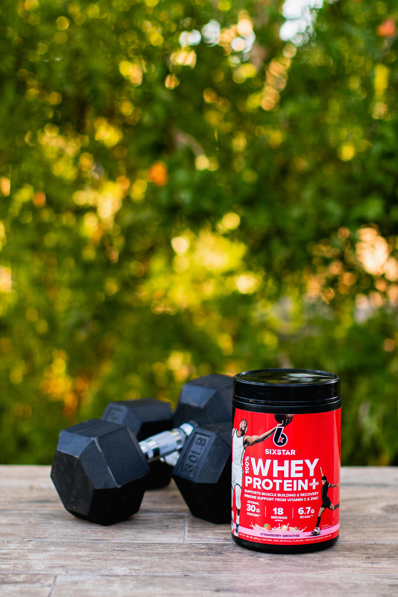 Protein powder jar with dumbbells in the background