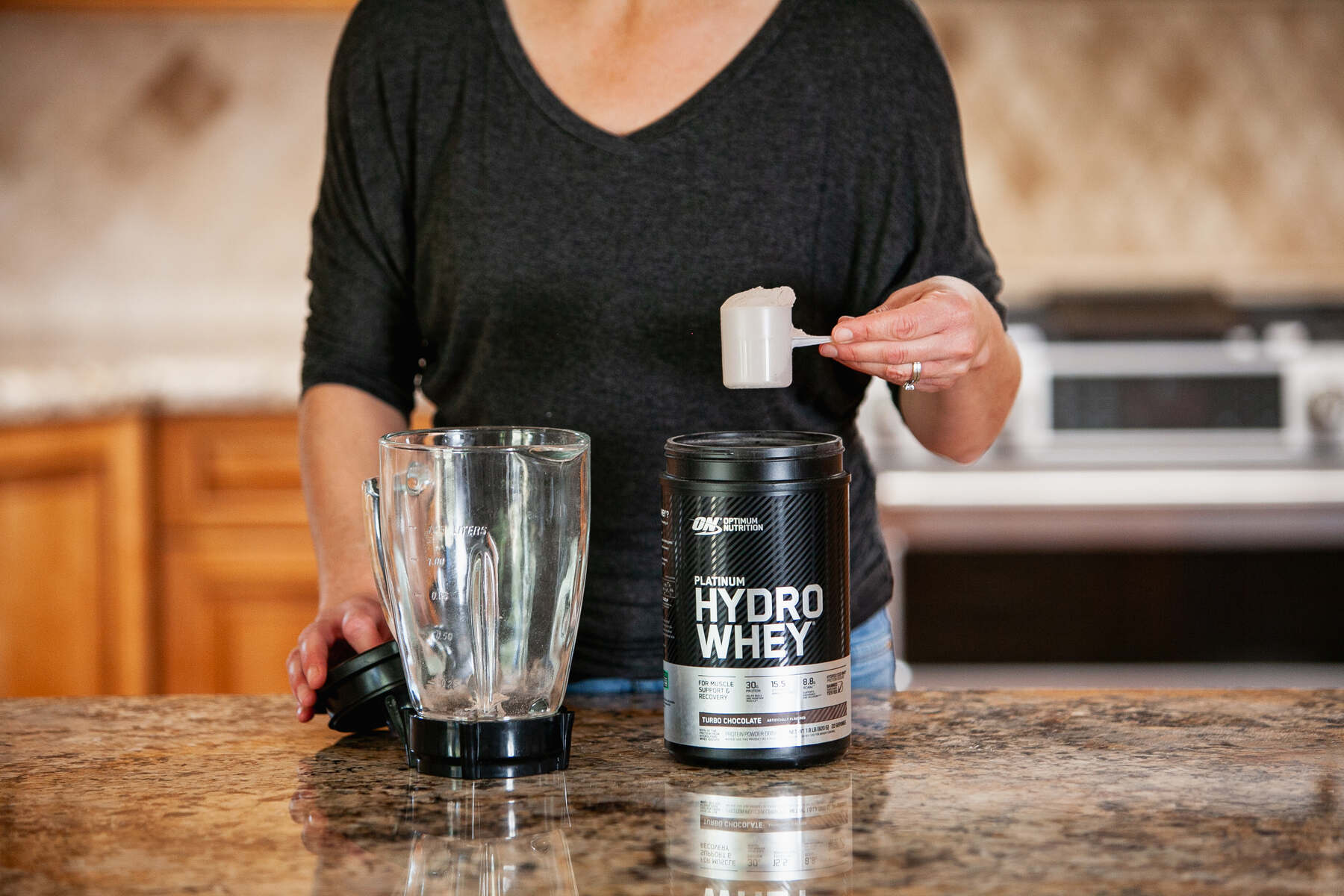 A woman scooping protein powder into a blender on a kitchen counter
