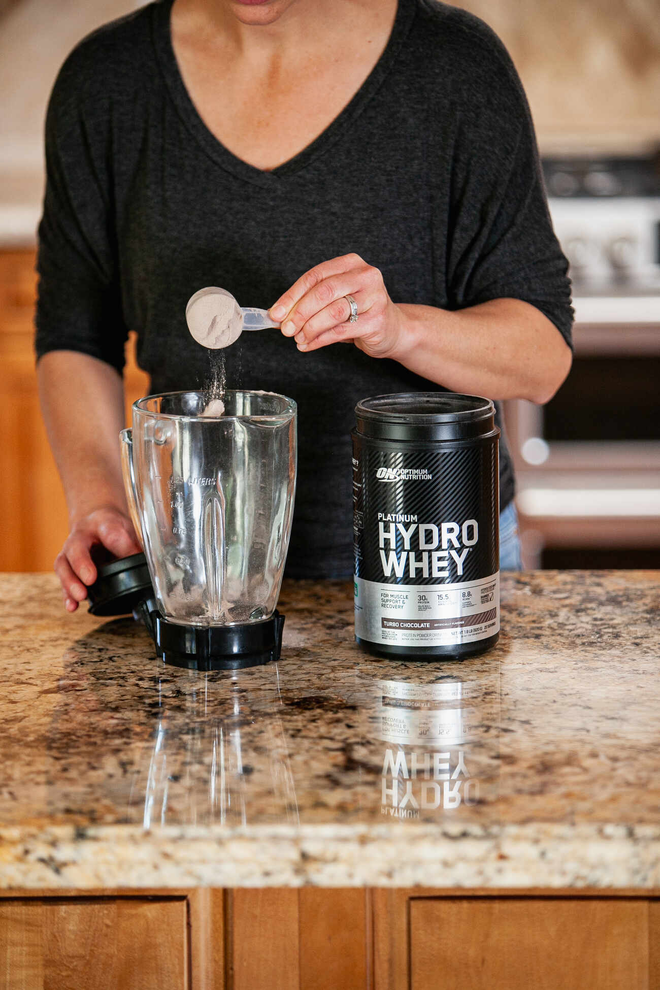 A woman scooping powder into blender beside protein container