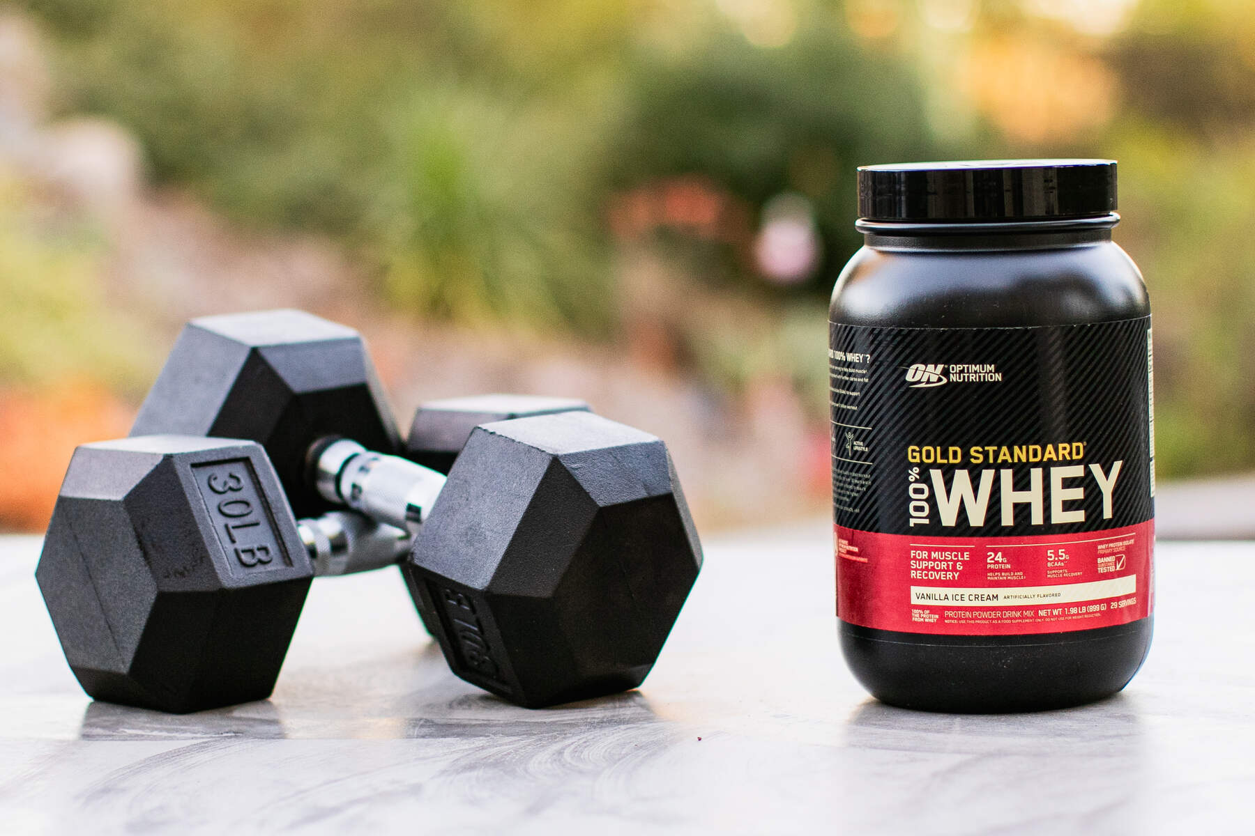 Whey protein container and dumbbells on an outdoor surface