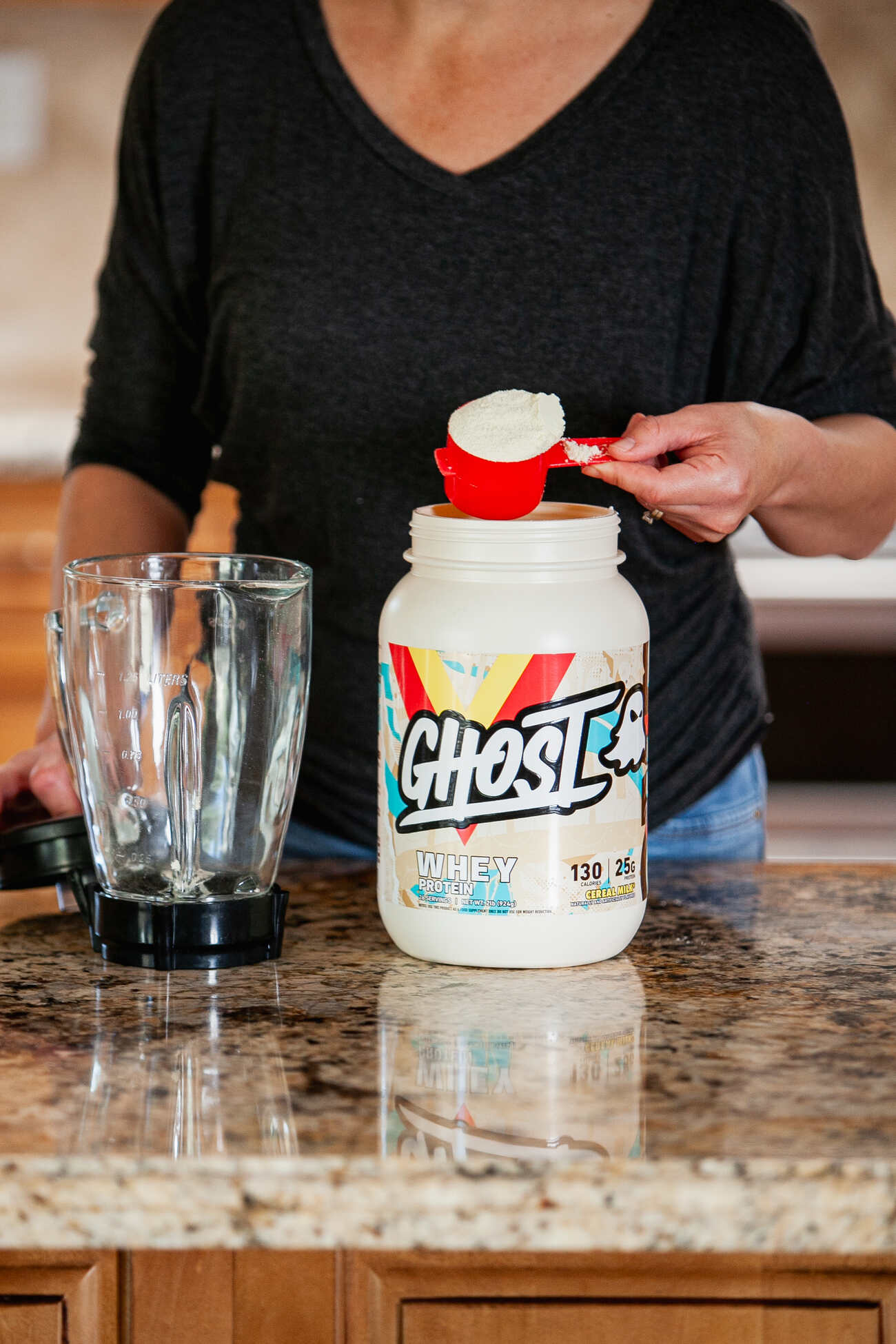 A woman adding whey protein to a blender for a shake