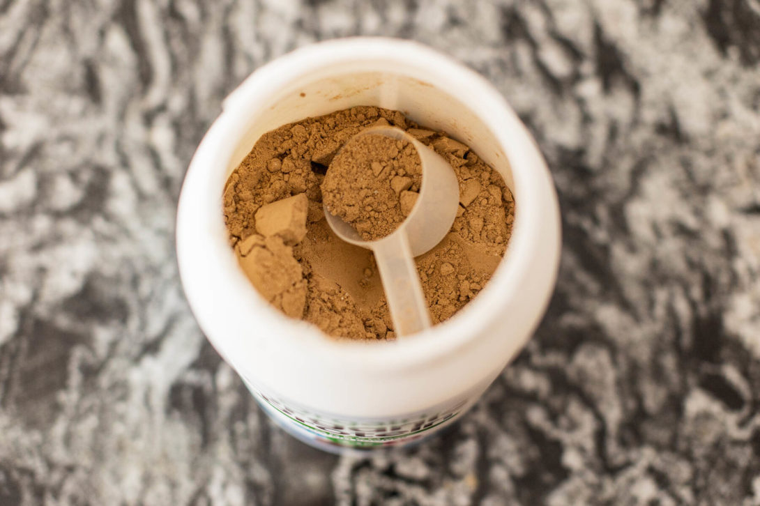 Top view of an open protein powder container showing a scoop resting on the powder surface