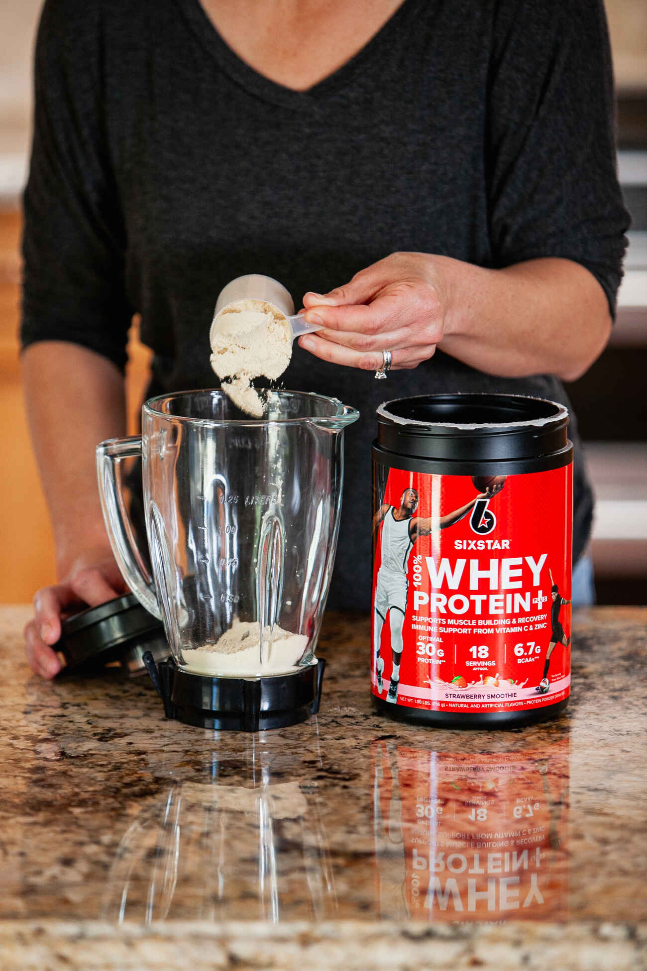 A woman adding whey protein to blender for shake preparation