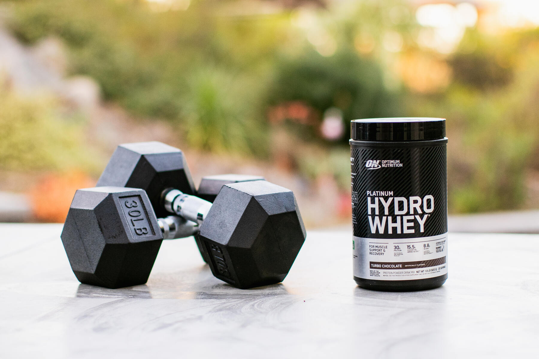 Whey protein container and dumbbells on an outdoor table
