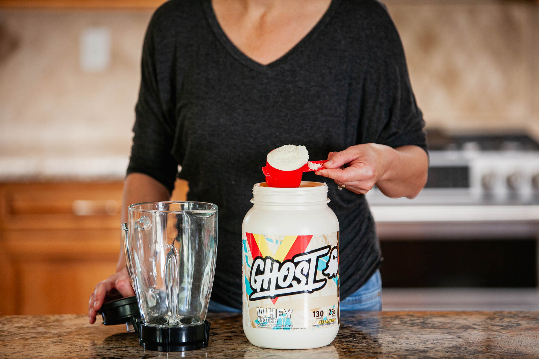 A woman scooping protein powder into a blender