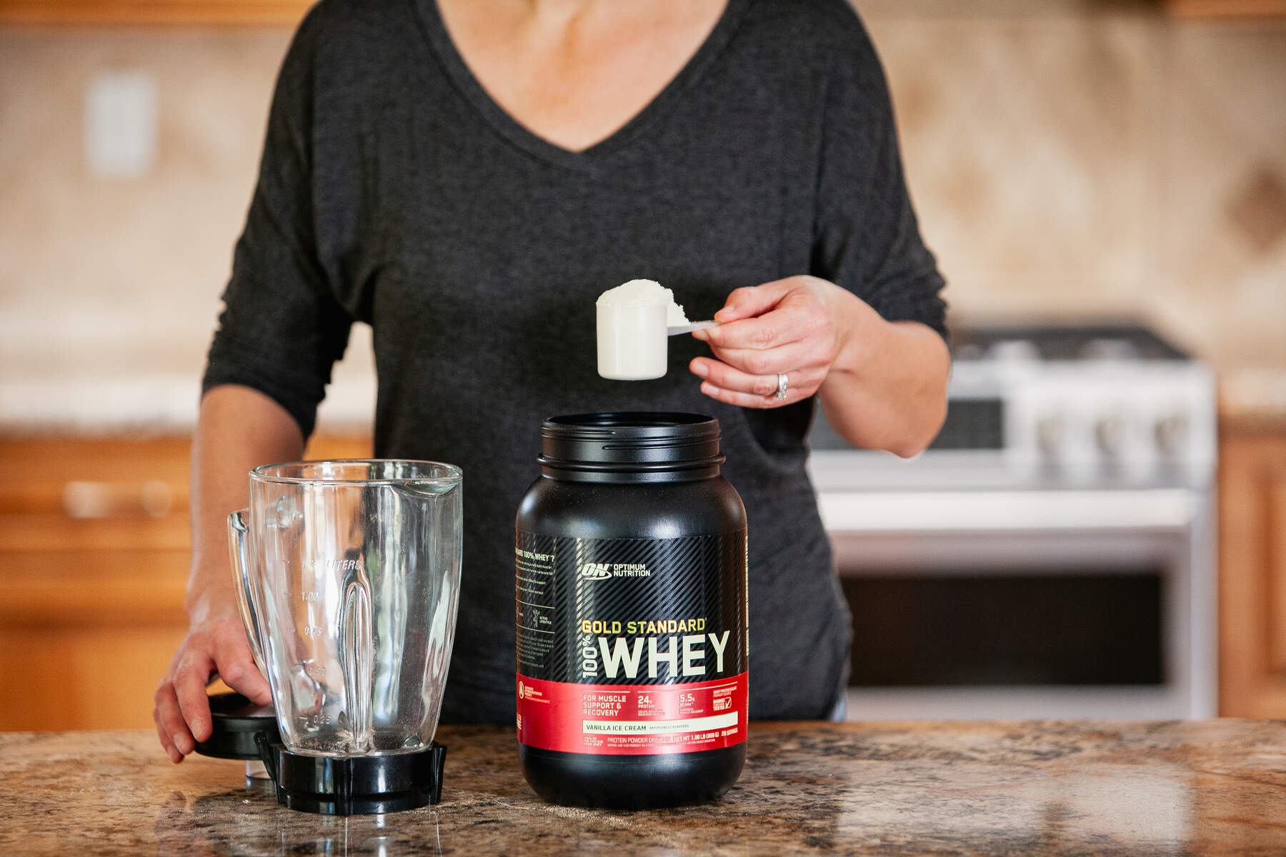 A woman scooping protein powder from a container into a blender