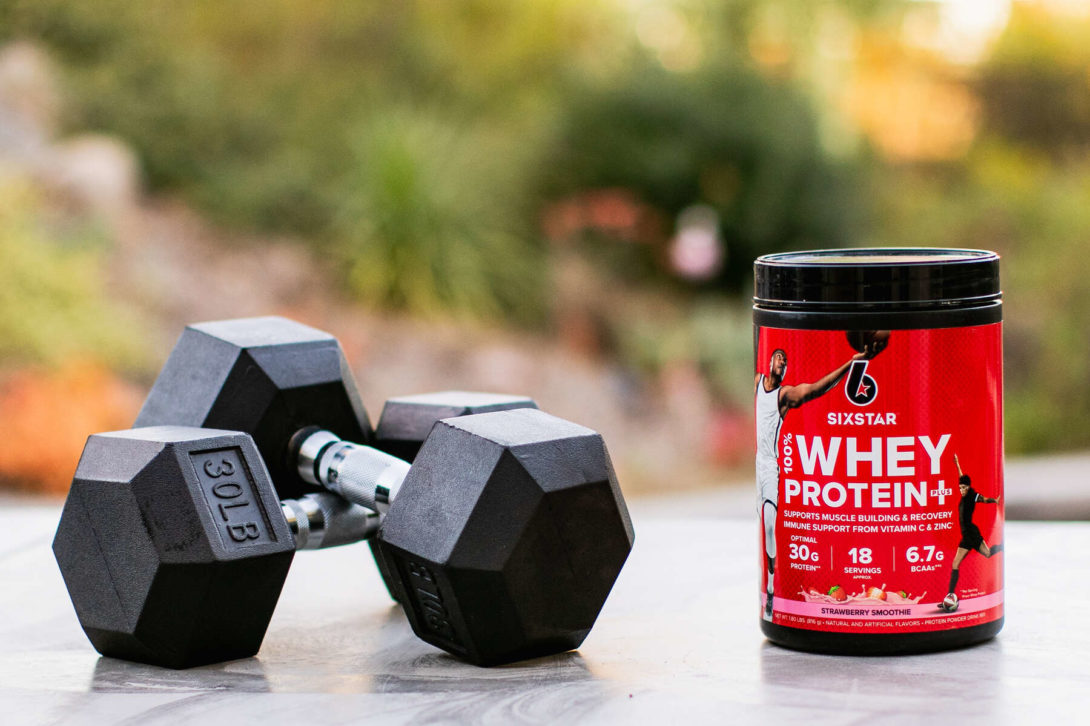 Dumbbells and a jar of whey protein powder on an outdoor marble surface