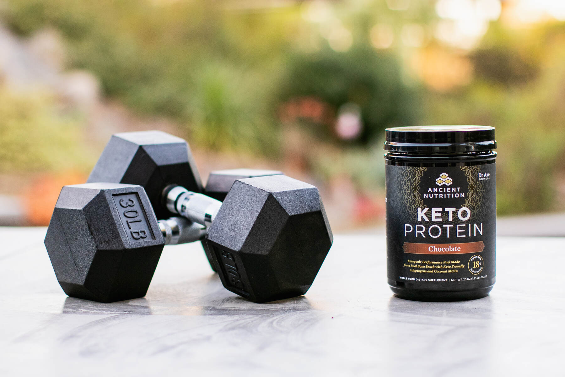 30lb dumbbells on a concreate table next to a container of Ancient Nutrition Keto Protein