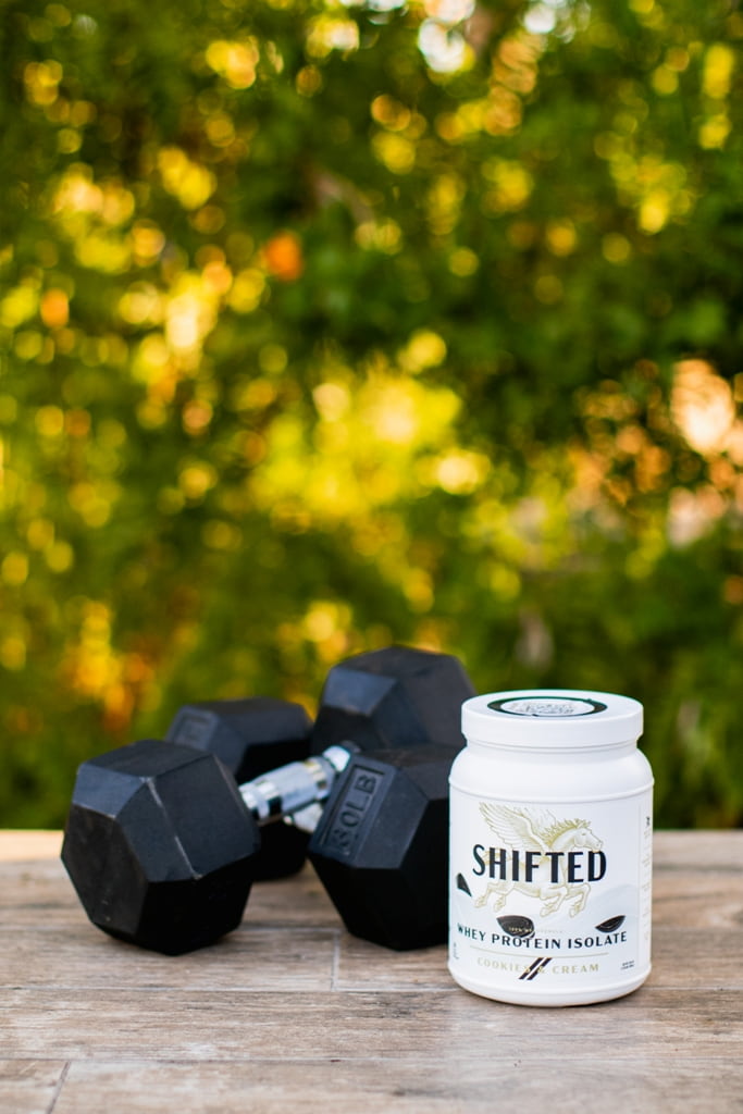 SHIFTED Whey Protein Isolate beside a pair of dumbbells
