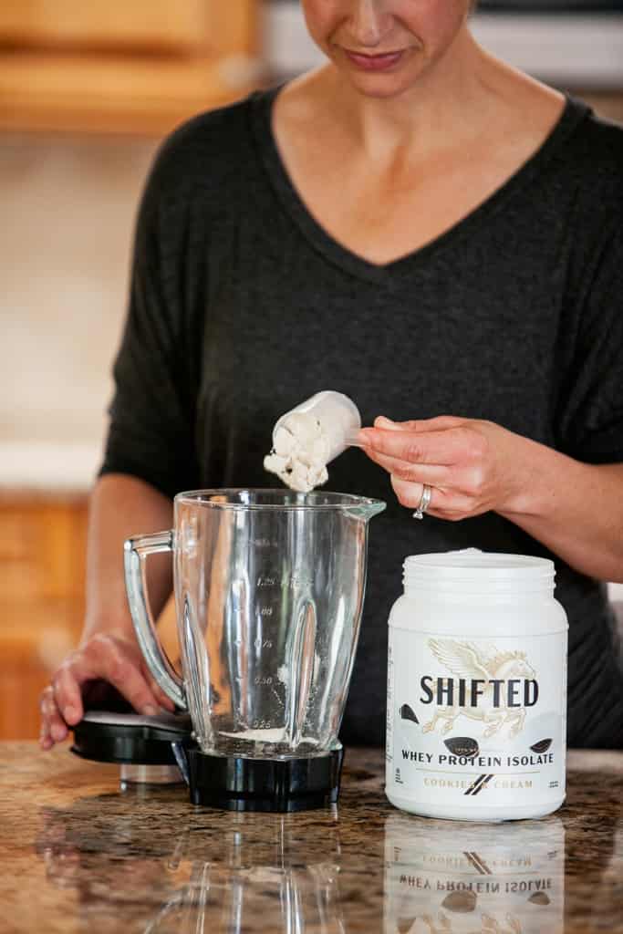 Woman pouring out a scoop of Shifted protein powder on a blender