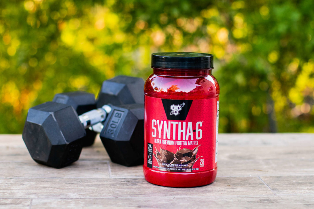 SYNTHA-6 protein container beside dumbbells on an outdoor wooden table
