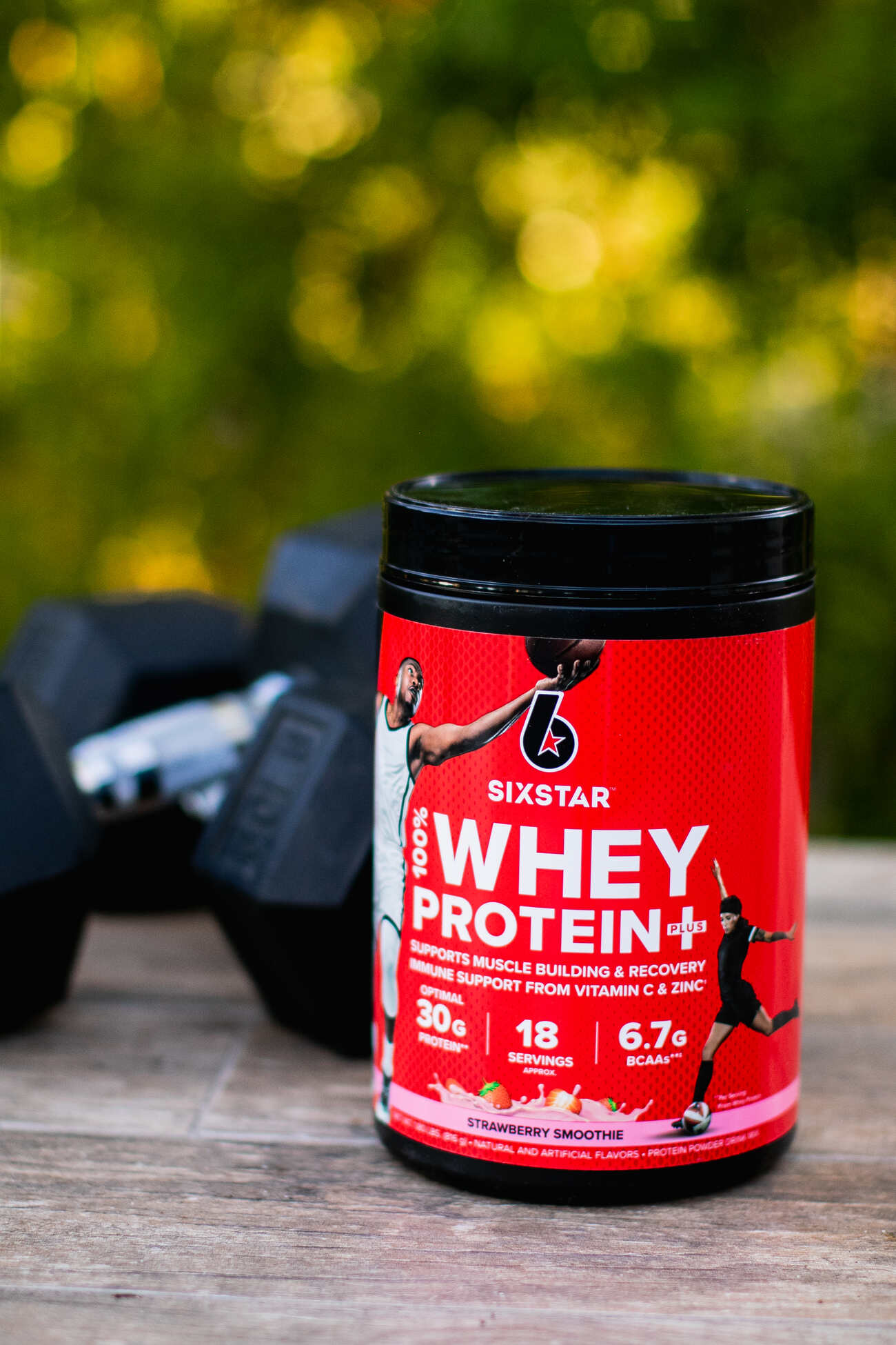 Strawberry whey protein container with dumbbells in background