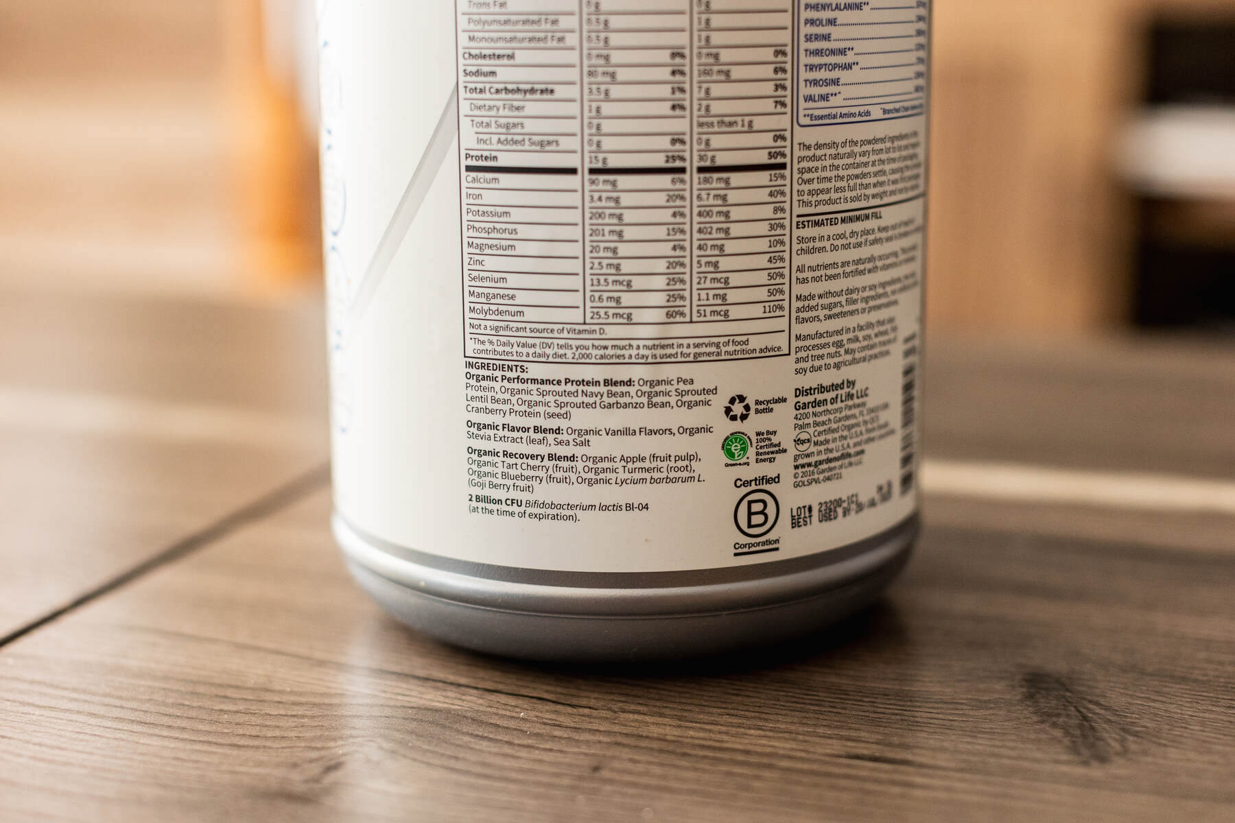 Ingredients label and nutrition content for a container of protein powder on a wooden coffee table