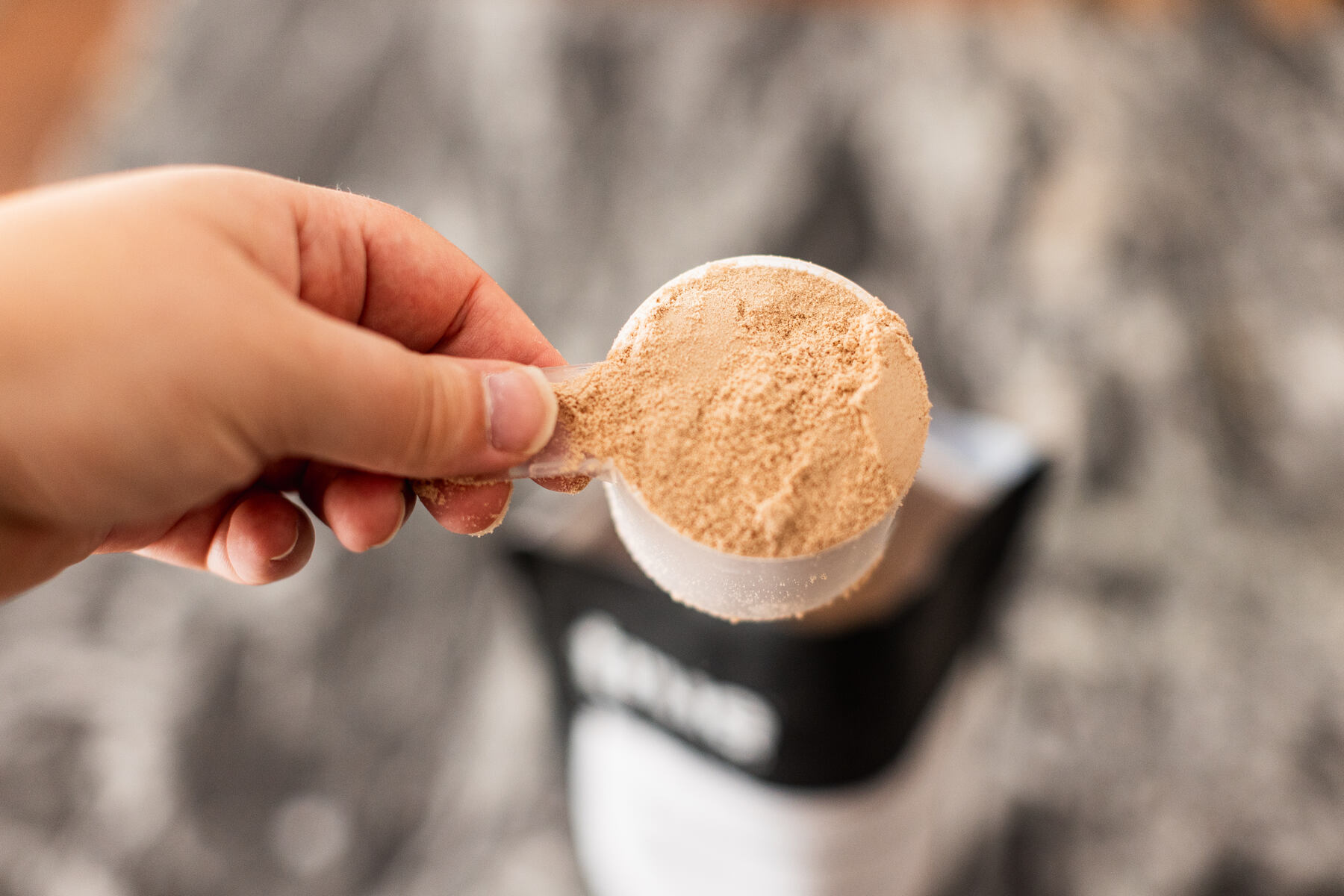 Person holding a scoop of whey protein powder over a black and white granite countertop
