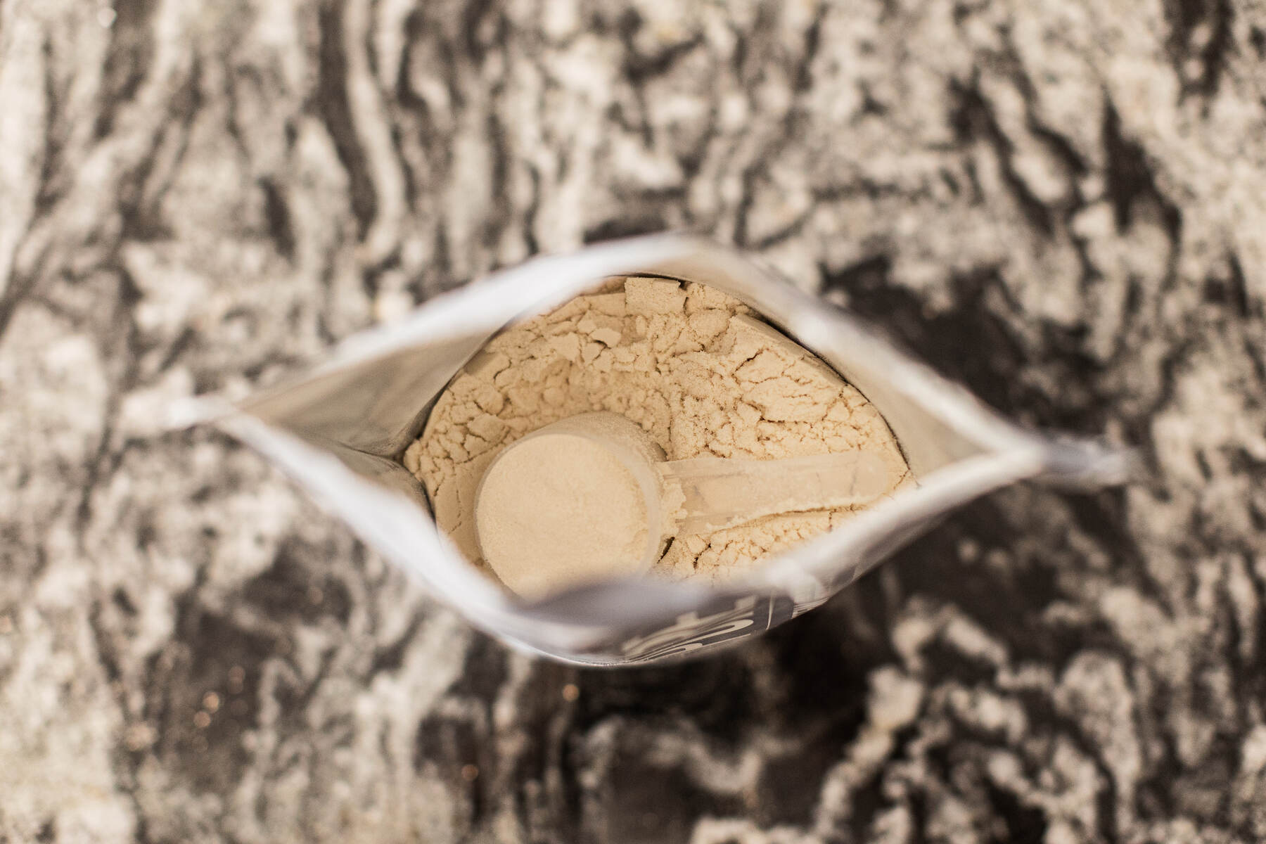 Open bag of whey protein powder with a scoop inside, on a marbled surface