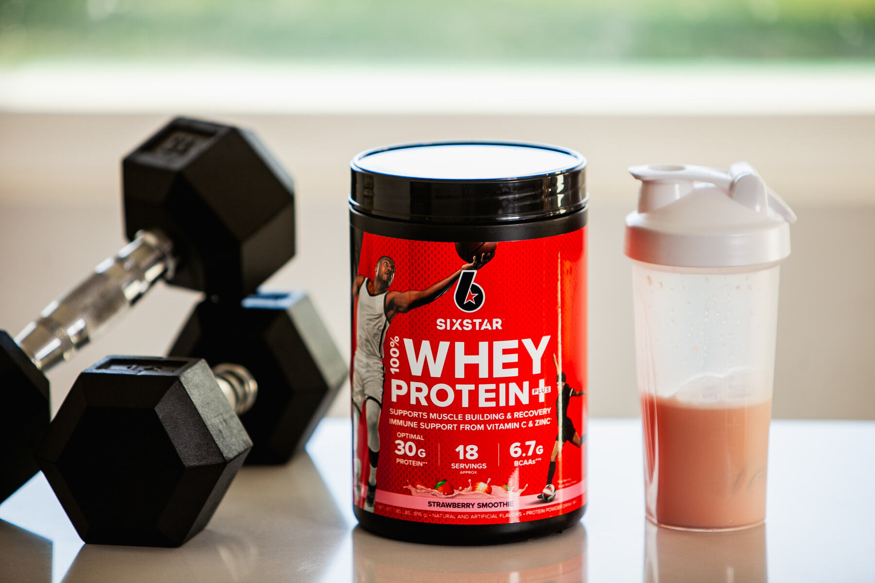 Whey protein and shaker bottle next to dumbbells